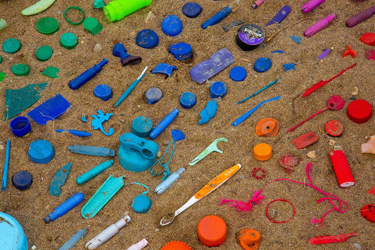 Plastikmüll nach Farben sortiert im Sand.