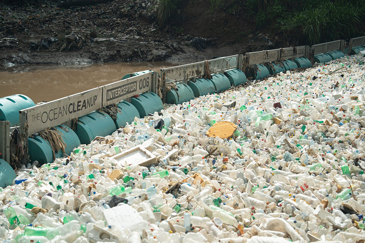 Ein Fluss mit einer Barrikade aus schwimmenden Tonnen, die abertausende weiße Plastikflaschen zurückhält.
