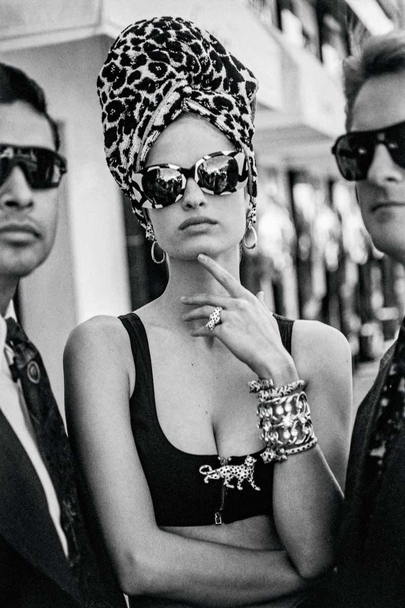 Modefotografie: Frau in schwarzem Kleid mit markantem Panthère-Schmuck posiert, flankiert von zwei im Bild angeschnittenen Bodyguards, vor hellem Hintergrund; Aufnahme für Vogue Italia, März 1992.