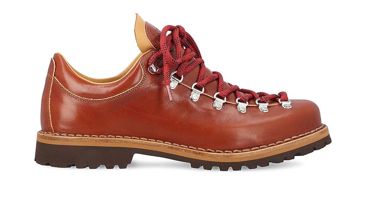 Brauner Lederschnürschuh im Bergsteigerstil, Seitenansicht, rote Rundschnürsenkel durch metallische Haken und Ösen, kräftige Profilsohle, rahmengenähte Naht sichtbar, freigestellt vor weißem Hintergrund.