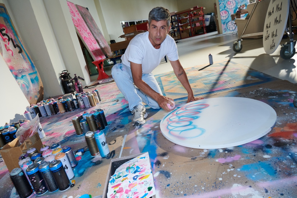 Graffiti-Künstler André Saraiva in seinem Atelier, umgeben von Spraydosen, arbeitet an einer runden Leinwand