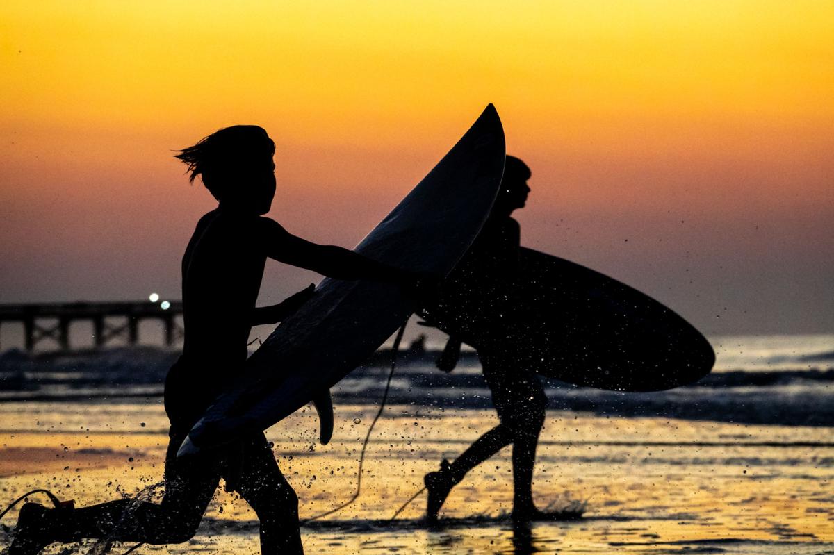 Junge Surfer rennen bei Sonnenaufgang ins Meer, um die ersten Wellen des Morgens zu erwischen.