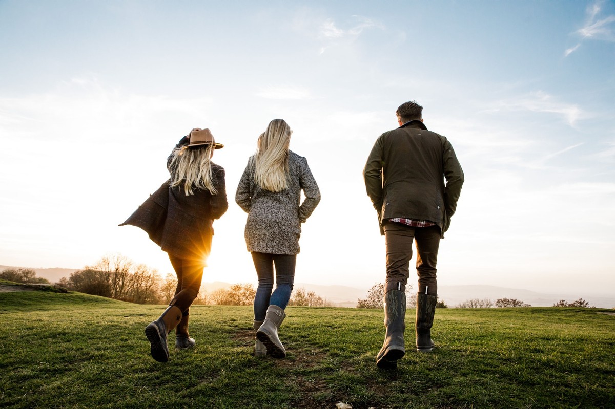 Drei Personen spazieren bei Sonnenuntergang über eine Wiese, alle tragen Muck Boots.