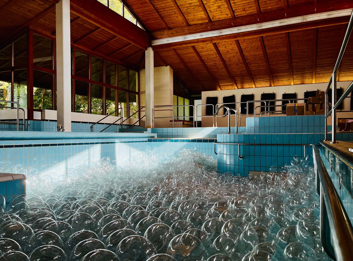 substantial-times-zahl-der-woche-1111-glaeserne-bubbles-badehaus-maiersreuth-02 Poolraum des ehemaligen Badehauses Maiersreuth mit holzverkleidetem Dach und türkisfarbenen Kacheln. Das leere Schwimmbecken ist dicht gefüllt mit hunderten gläsernen Kugeln der Installation „Effervescent“ von Louise Lang.