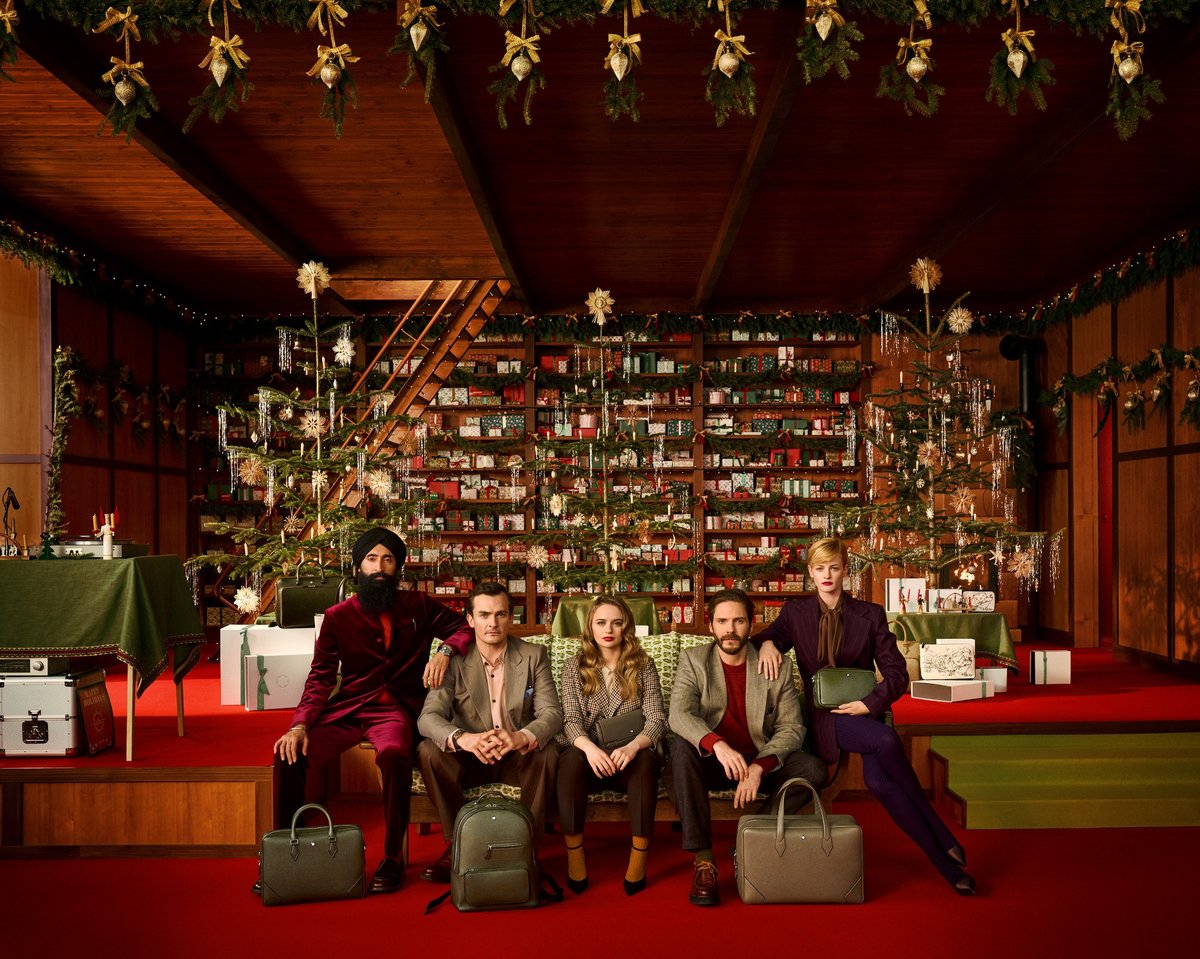 Fünf Hollywood-Schauspielerinnen und -Schauspieler sitzen in einer festlich dekorierten, holzgetäfelten Bibliothek nebeneinander. Hinter ihnen stehen mehrere Christbäume und Regale voller Geschenkboxen. Von links nach rechts sind zu sehen: Waris Ahluwalia, Rupert Friend, Joey King, Daniel Brühl und Esther McGregor.