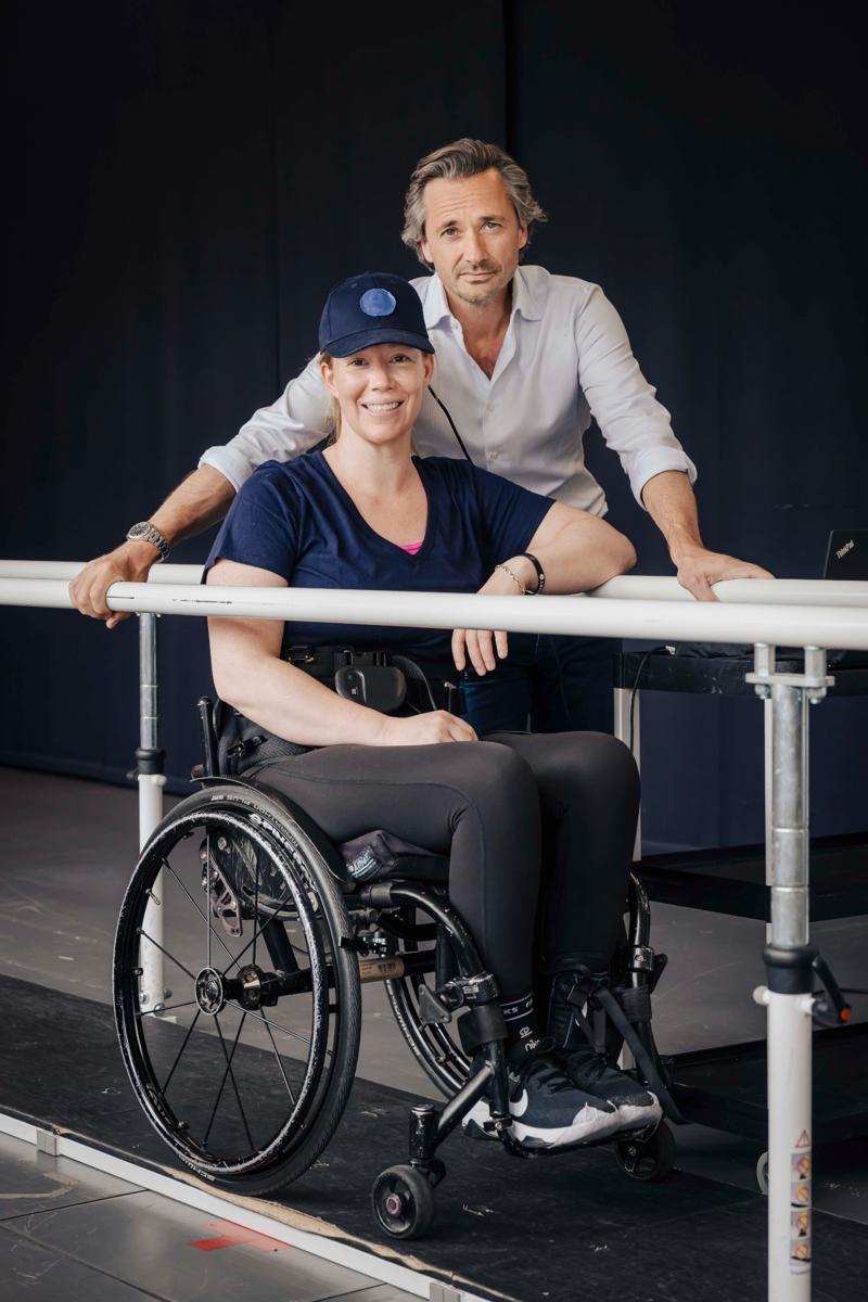 substantial-times-die-bruecke-ueber-das-unmoegliche-gregoire-courtine-rolex-award-04 Suzanne Edwards sitzt in einem Rollstuhl und lächelt, während Grégoire Courtine hinter ihr steht und sich leicht über die Stange lehnt, an der sie gerade ihre ersten Schritte gemacht hat; beide befinden sich in einem Rehabilitationslabor.