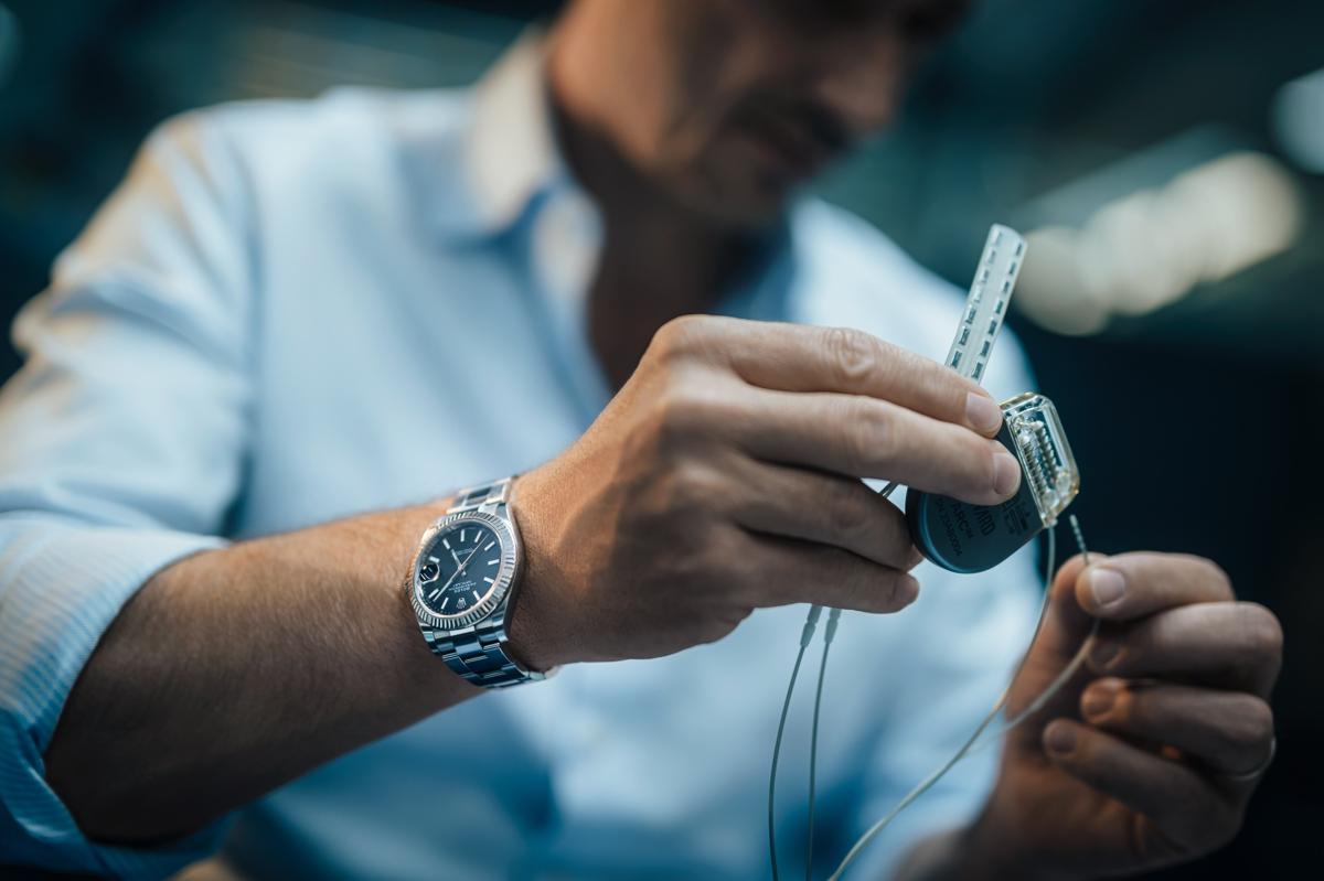substantial-times-die-bruecke-ueber-das-unmoegliche-gregoire-courtine-rolex-award-06 Nahaufnahme von Grégoire Courtines Händen, wie er ein medizinisches Implantat und eine Elektrodenleiste prüft; der Hintergrund ist unscharf, der Fokus liegt auf dem Gerät und seinem präzisen Arbeiten.