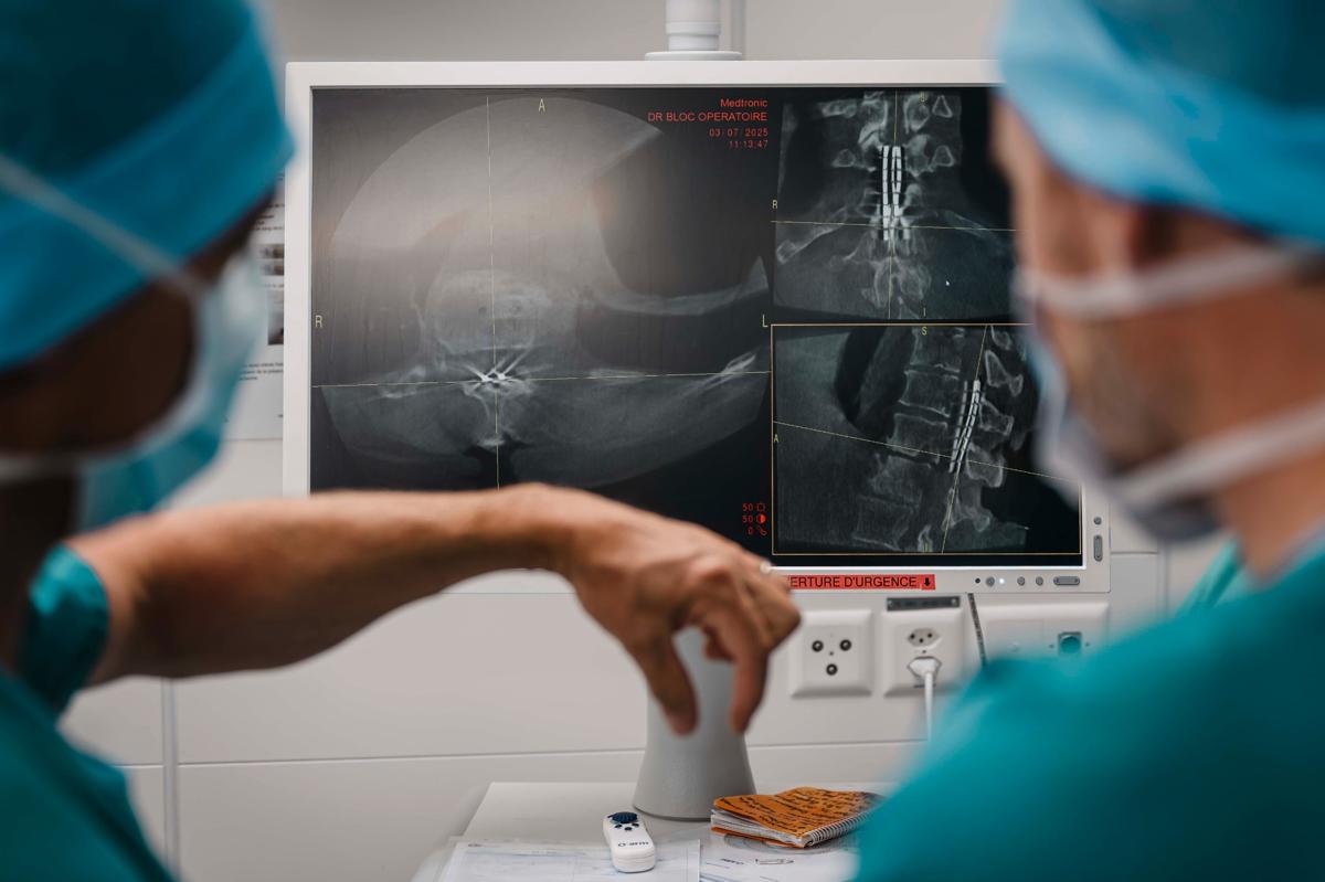 substantial-times-die-bruecke-ueber-das-unmoegliche-gregoire-courtine-rolex-award-10 Jocelyne Bloch und Grégoire Courtine betrachten nach einer Operation Röntgen- und CT-Aufnahmen einer Wirbelsäule; die Scans zeigen implantierte Elektroden, während beide Ärztinnen und Ärzte in OP-Kleidung vor dem Monitor stehen.