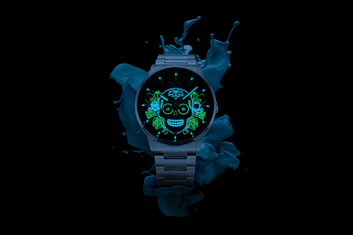 substantial-times-mehr-zeit-als-wir-03 Schwarze Mido Commander Uhr mit leuchtendem Totenkopf-Motiv auf dem Zifferblatt. Die fluoreszierende Gravur in Türkis und Grün erinnert an die mexikanischen „Calaveras“ des Día de los Muertos und hebt sich eindrucksvoll vom dunklen Hintergrund ab.