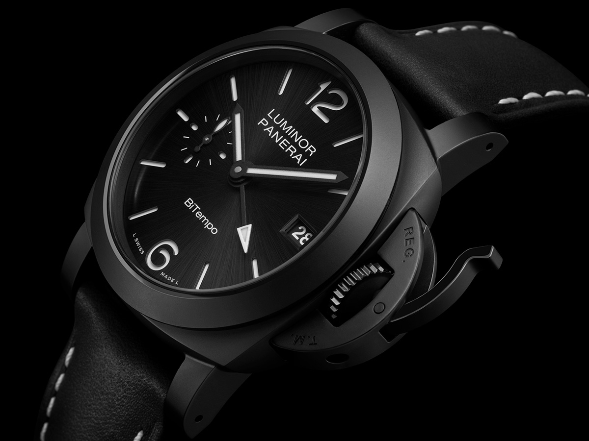 substantial-times-mehr-zeit-als-wir-06 Nahaufnahme einer Armbanduhr von Panerai, Modell Luminor GMT Ceramica PAM01460. Die Uhr hat ein schwarzes Keramikgehäuse mit Kronenschutzbrücke, ein schwarzes Zifferblatt mit Sonnenschliff und weißen Leuchtziffern sowie Zeigern. Bei 9 Uhr befindet sich eine kleine Sekundenanzeige, bei 3 Uhr ein Datumsfenster. Die Uhr ist an einem schwarzen Lederarmband mit weißen Ziernähten befestigt.