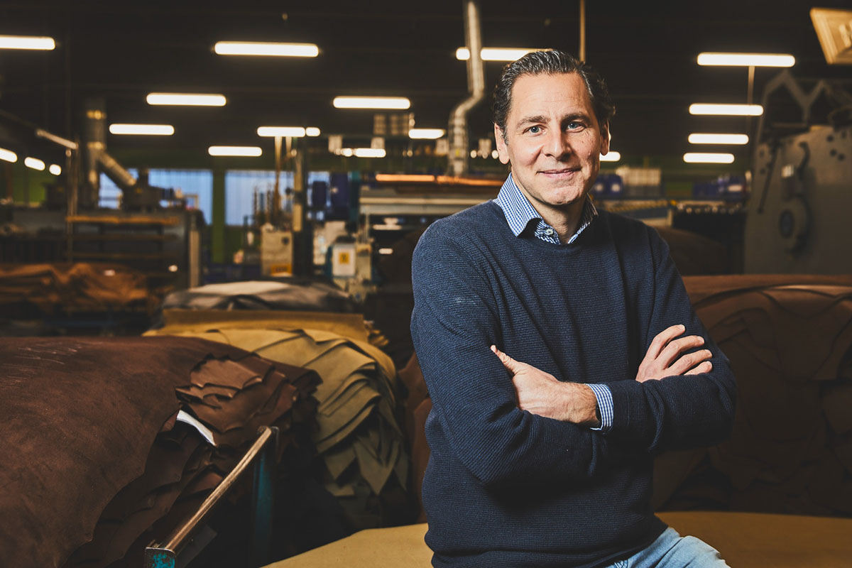 substantial-times-wir-haben-verlernt-materialien-mit-wuerde-zu-behandeln-02 Thomas Heinen sitzt mit verschränkten Armen auf einem Lederstapel in der Produktionshalle der Gerberei, umgeben von gestapelten Lederhäuten.