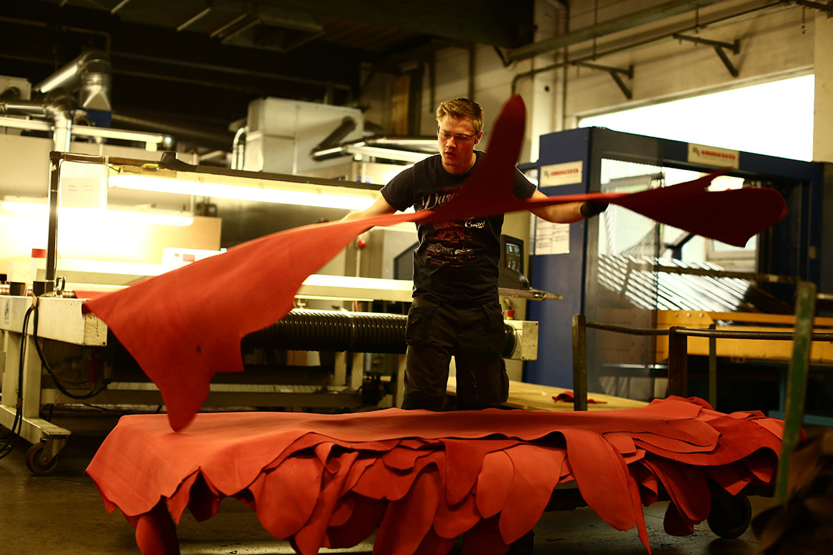 substantial-times-wir-haben-verlernt-materialien-mit-wuerde-zu-behandeln-07 Ein Mitarbeiter legt frisch gespritzte rote Lederstücke auf einen Transportwagen, nachdem sie aus der Spritzanlage kommen.