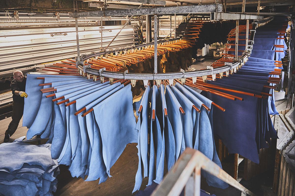 substantial-times-wir-haben-verlernt-materialien-mit-wuerde-zu-behandeln-08 Blaue Lederhäute hängen in der Hängetrocknung der Gerberei Heinen, während ein Mitarbeiter frische Häute einlegt.