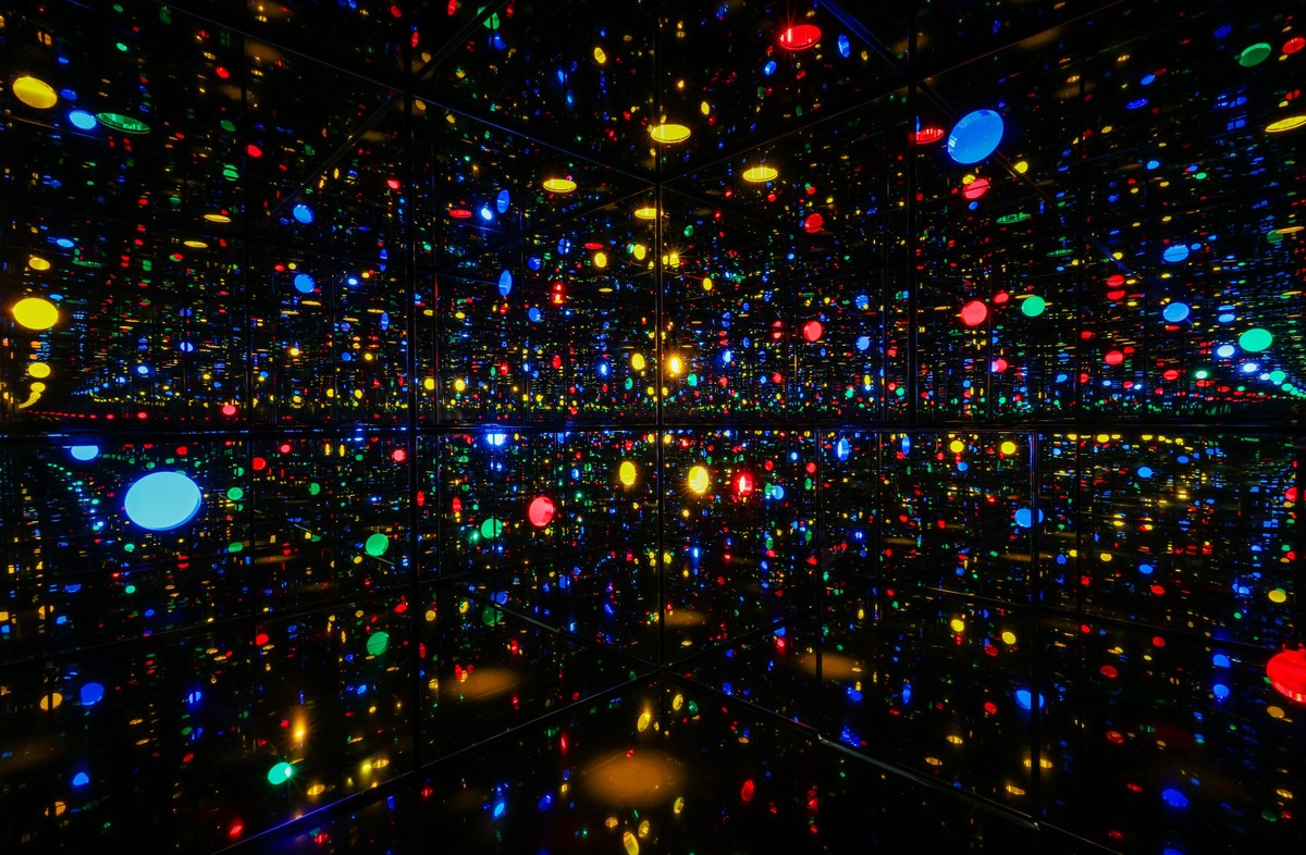 substantial-times-yayoi-kusama-nichts-hat-ein-ende-07 Innenansicht eines spiegelverkleideten Raums mit farbigen Lichtpunkten in Rot, Gelb, Grün und Blau, die sich unendlich in alle Richtungen vervielfachen.