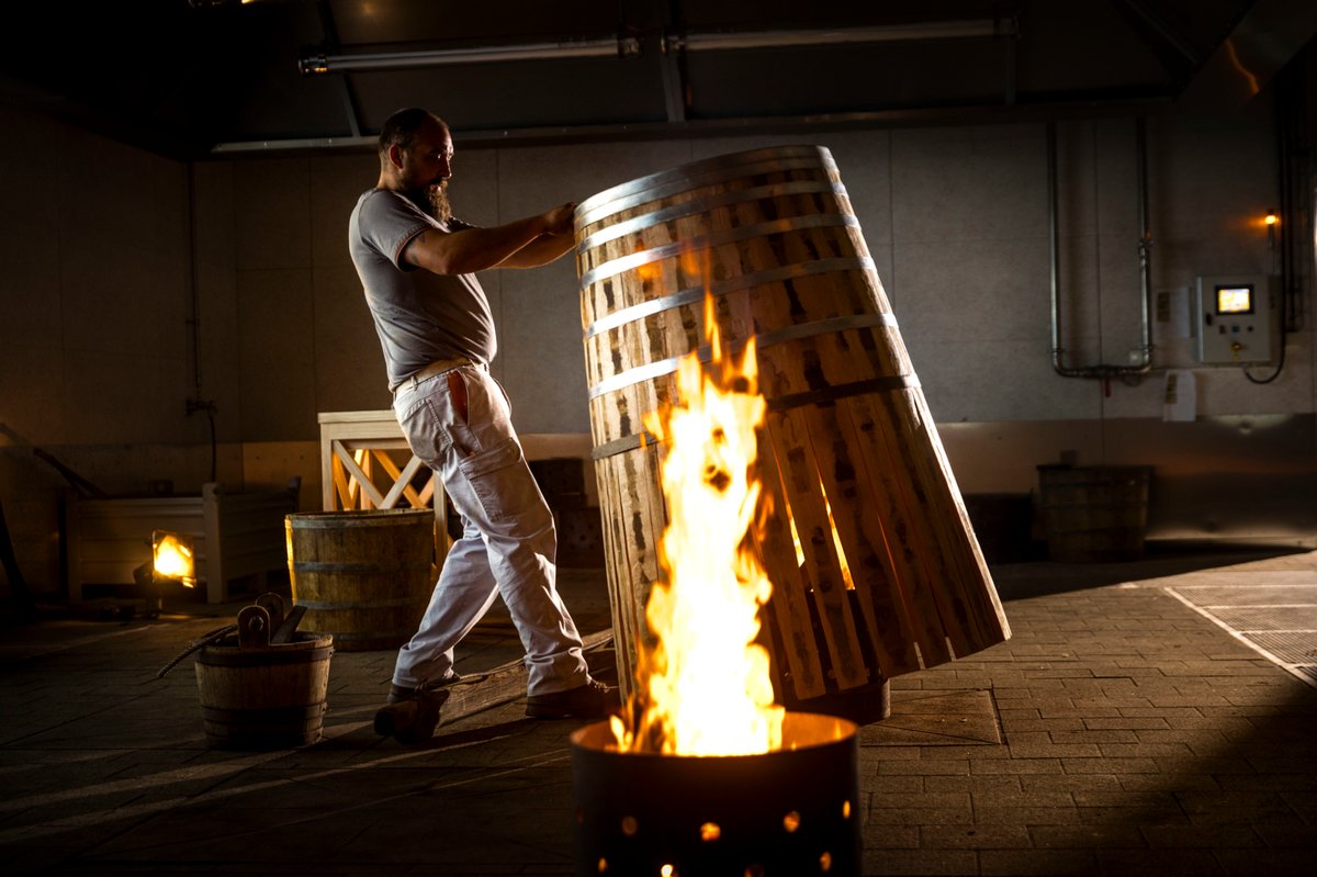 Ein Fassbinder erhitzt ein Holzfass über offenem Feuer in der Tonnellerie.