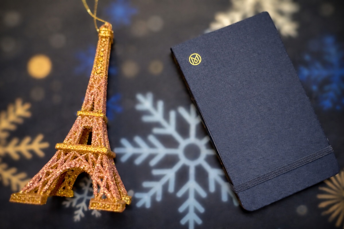 Blaues Notizbuch, dekoriert mit zwei Filzsternen in Rot- und Orangetönen, liegend auf dunkelblauem Stoff mit weihnachtlichen Symbolen wie Sternen und Kreisen.