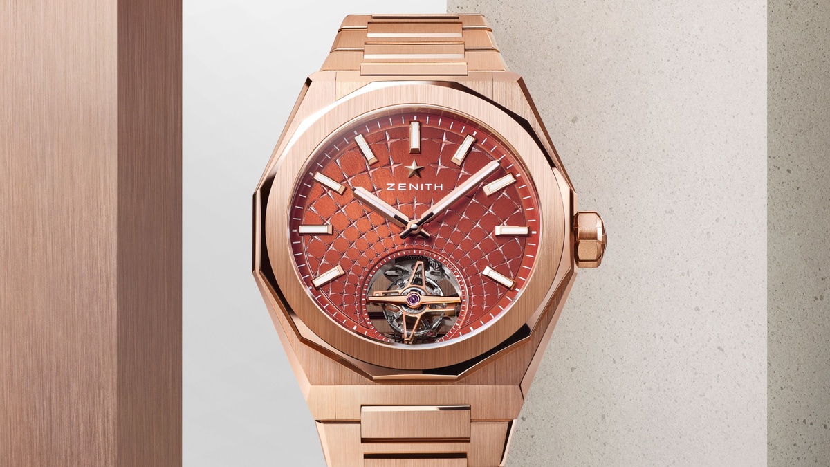Roségoldene Zenith-Armbanduhr mit ziegelrotem, sternförmig strukturiertem Zifferblatt und offenem Tourbillon bei 6 Uhr, frontal vor einer minimalistischen Architektur aus Metall- und Steinflächen präsentiert.