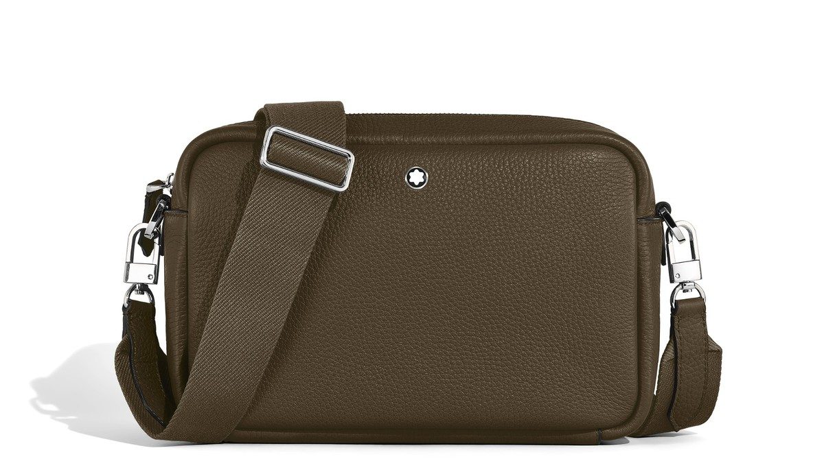 Eine rechteckige Crossbody-Tasche von Montblanc in der grünbraunen Farbe Noisette, gefertigt aus genarbtem Leder. Die Tasche hat einen breiten, verstellbaren Schulterriemen aus textiler Struktur, silberglänzende Karabiner und einen kleinen weißen Montblanc-Stern auf der Vorderseite. Das Produkt steht freigestellt vor weißem Hintergrund.