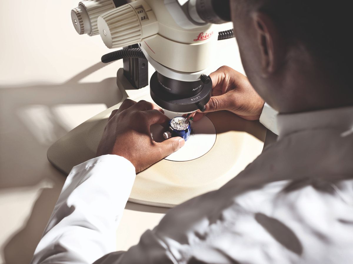 Feinmontage eines mechanischen Rolex Uhrwerks mit einer Pinzette unter einem Mikroskop.