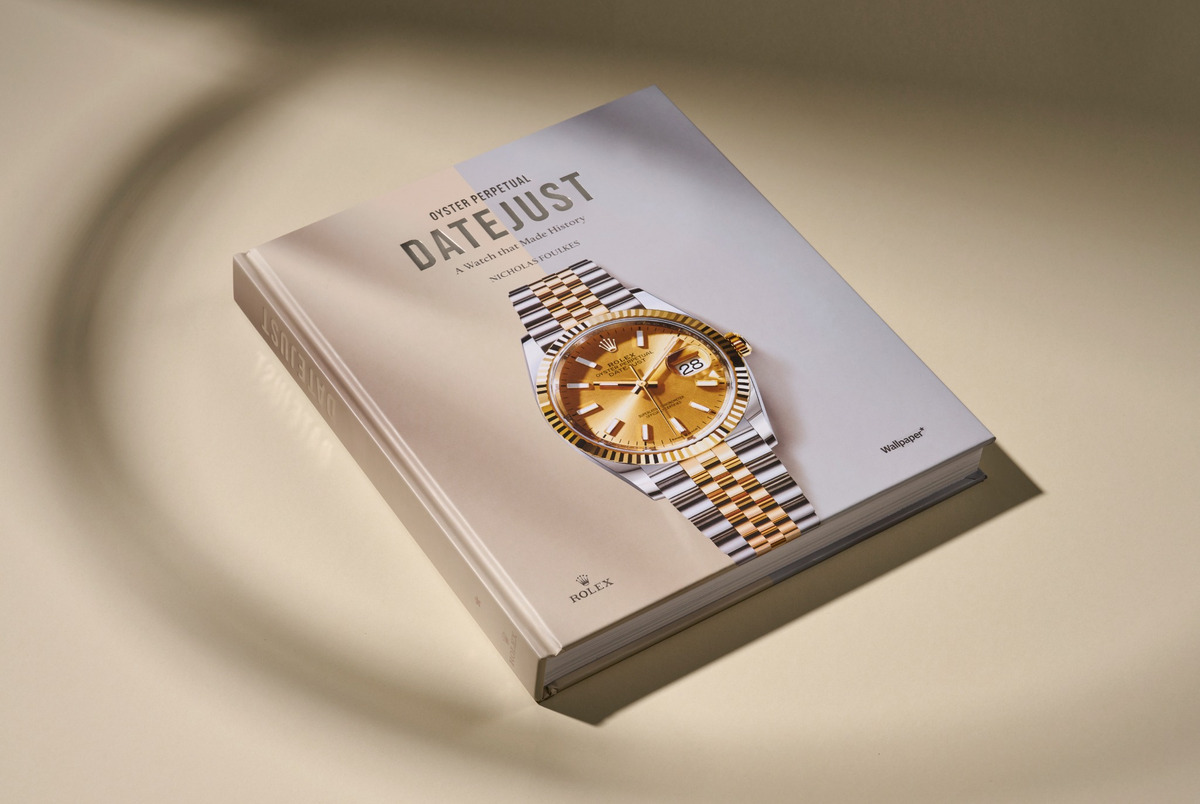 Hardcover-Buch „Oyster Perpetual Datejust – A Watch that Made History“ mit Abbildung einer Rolex Datejust Armbanduhr in Bicolor-Ausführung in Gold und Edelstahl, auf längs zweigeteiltem Hintergrund in Beige und Grau.