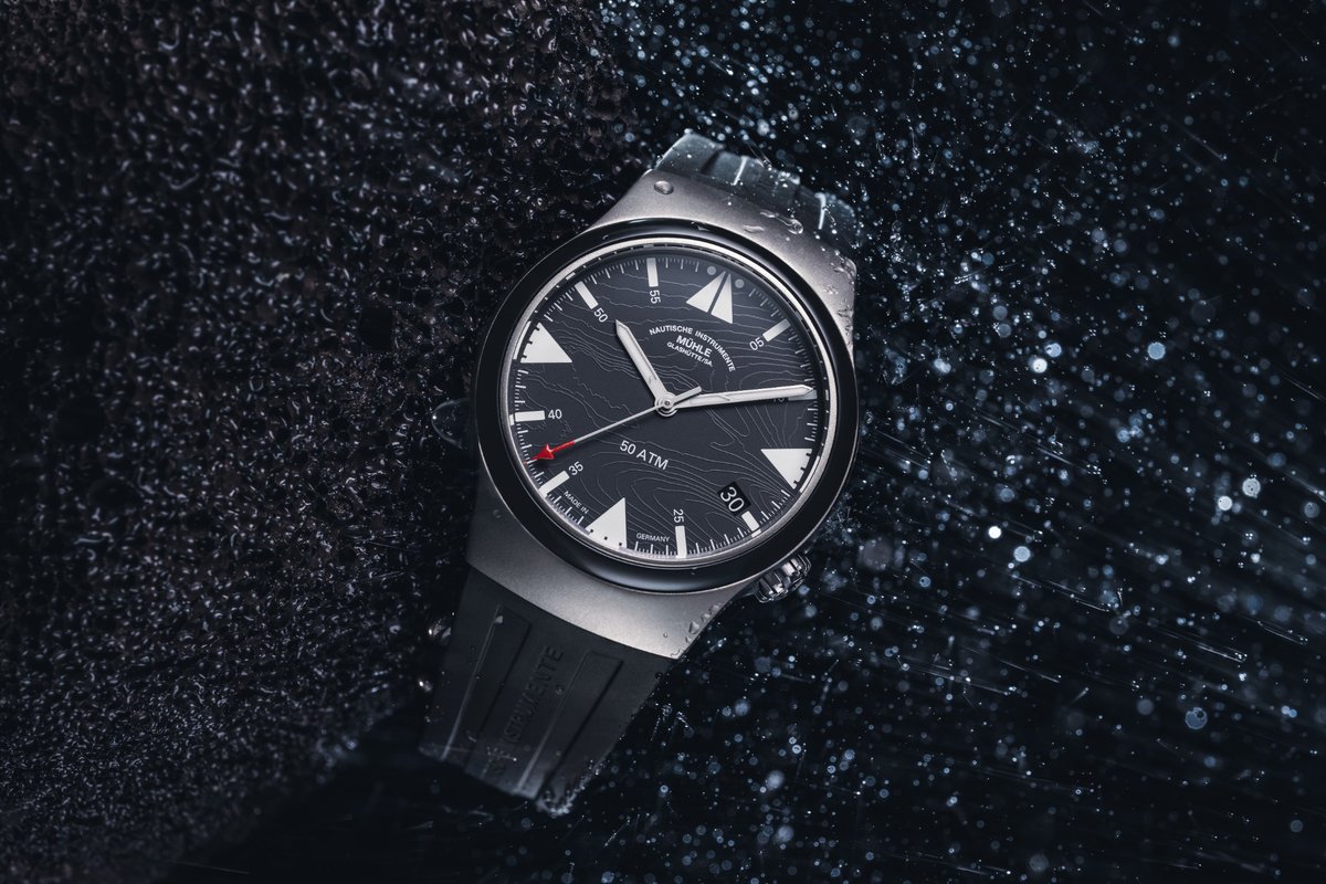 Sportliche Taucheruhr aus Titan von Mühle-Glashütte mit schwarzem Zifferblatt und roter Sekundenzeigerspitze auf nasser Steinoberfläche mit Reflektionen von Wasserspritzern