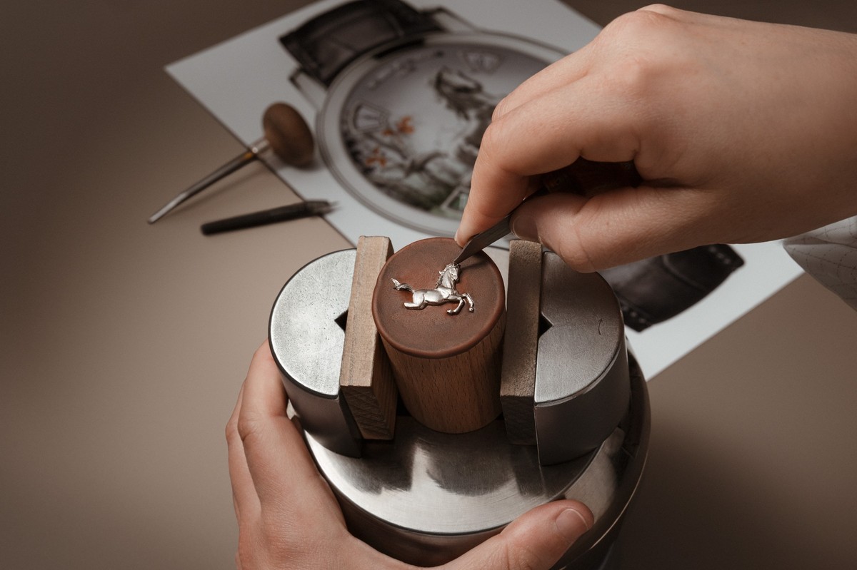 Hände eines Graveurs, der ein Pferdemotiv in eine Metallplatte graviert, mit Werkzeug und Detailansicht der entstehenden Reliefstruktur