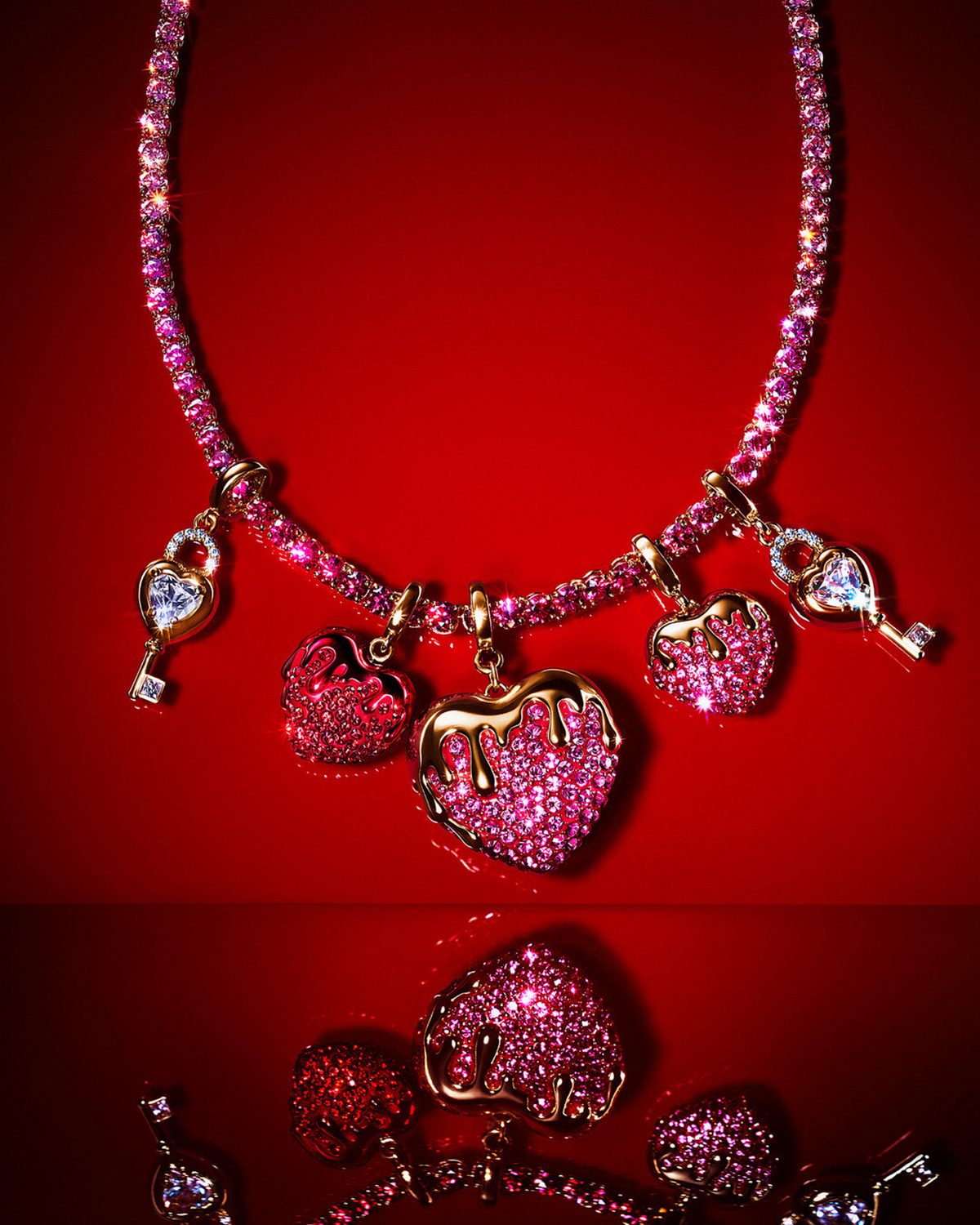 Rosa Tennis-Halskette mit mehreren Herzanhängern und Schlüsselmotiv, besetzt mit pinken und klaren Kristallen, auf rotem Hintergrund.