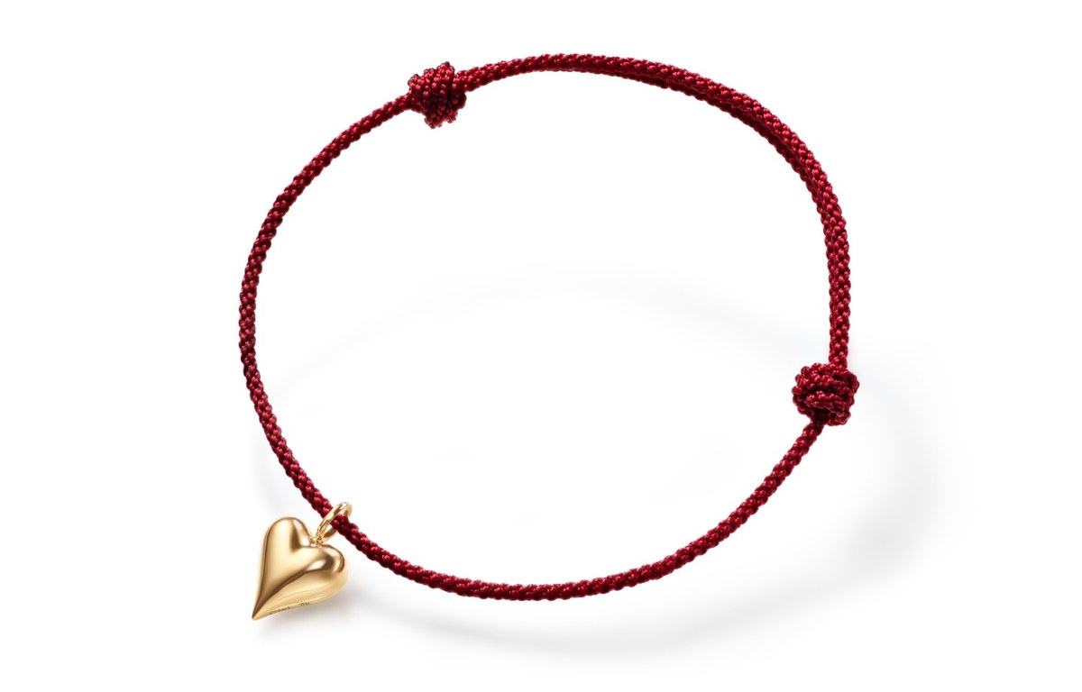 Rotes Kordelarmband mit verschiebbarem Knoten und herzförmigem Anhänger aus Gelbgold, auf weißem Hintergrund.