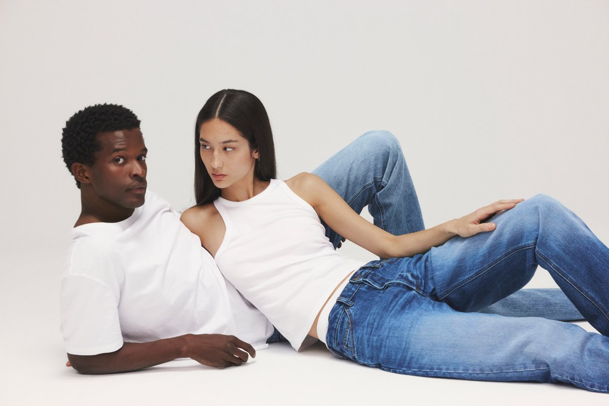 Zwei Models, ein Mann und eine Frau, liegen auf dem Boden und tragen Jeans und weiße Oberteile.