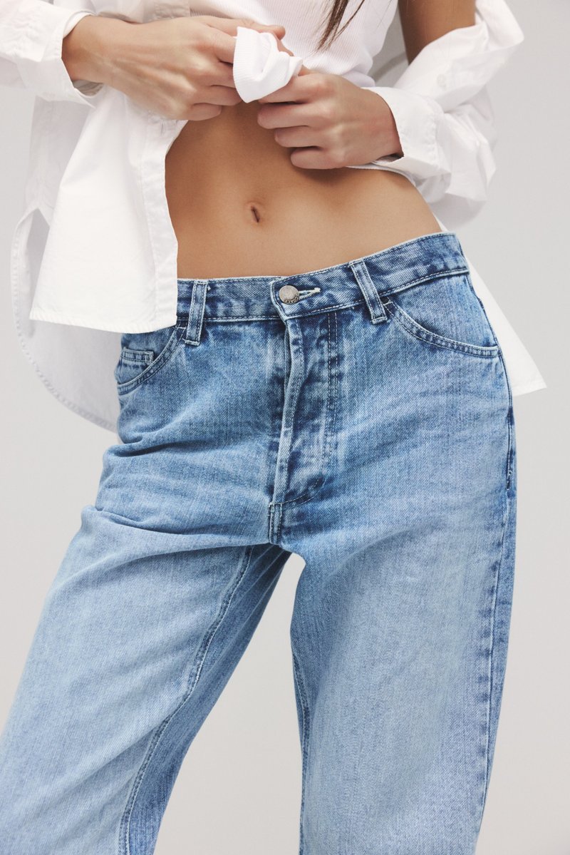 substantial-times-rebellion-der-revoluzzer-ecoalf-denim-06 Nahaufnahme Model, bauchfrei, mit offenem weißem Hemd und einer hellen Jeans mit sichtbarer Knopfleiste und Taschen