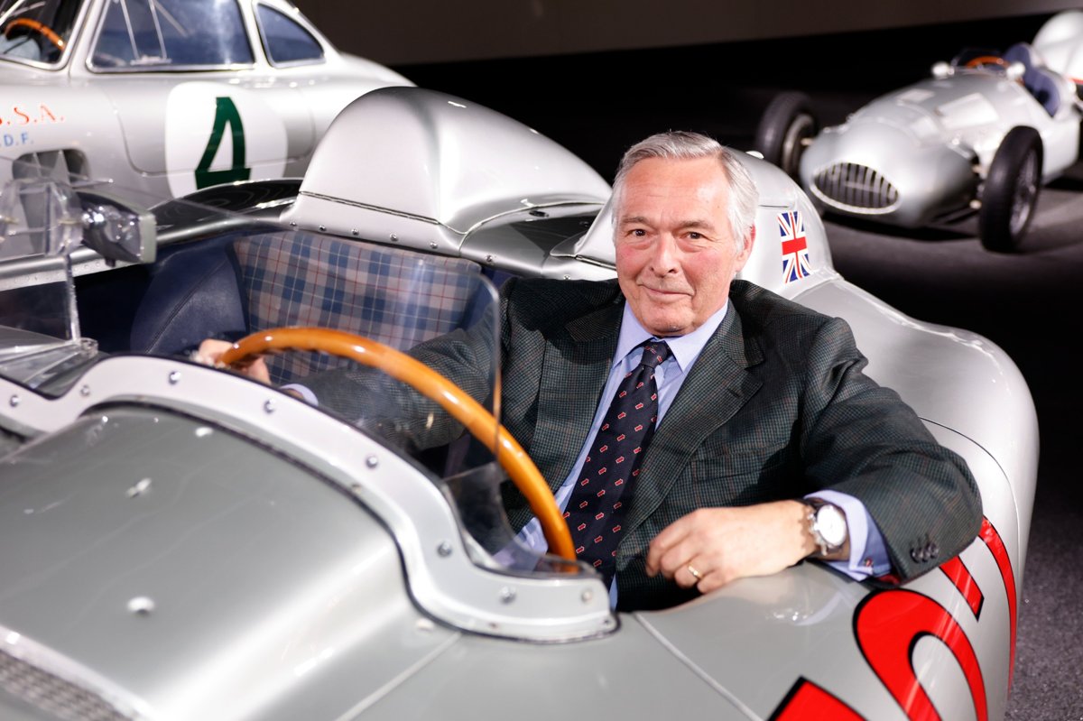 Karl-Friedrich Scheufele sitzt in einem silbernen historischen Rennwagen mit Holzlenkrad und der nummer 722, im Hintergrund weitere klassische Rennfahrzeuge