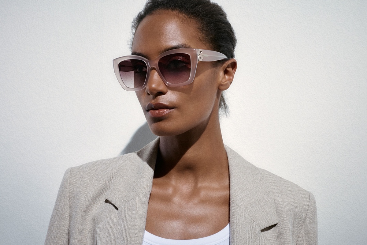 Frau mit zurückgebundenem Haar trägt eine roséfarbene Sonnenbrille mit großen Gläsern und hellen Rahmen