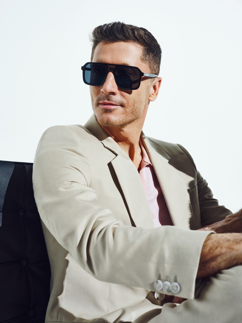 Mann im beigen Anzug trägt eine schwarze Sonnenbrille mit breitem Rahmen und blickt zur Seite