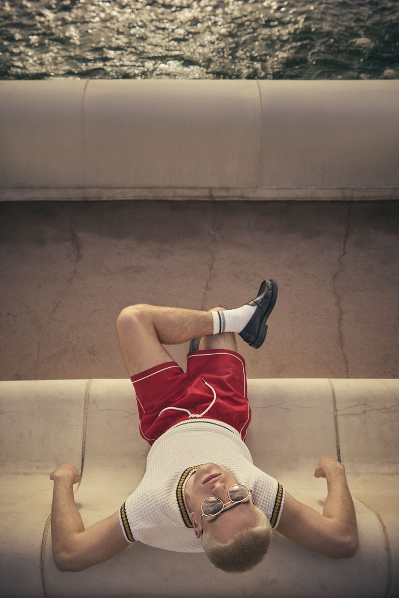 Mann lehnt auf einer Steinbank am Wasser und trägt runde Sonnenbrille mit Metallrahmen