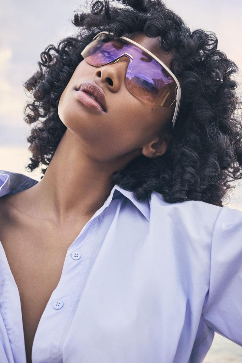 Frau mit lockigem Haar trägt große futuristische Sonnenbrille mit verspiegelten Gläsern