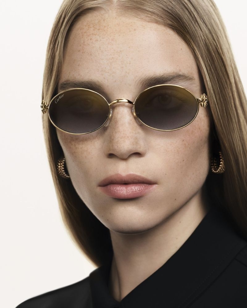 Frau mit Sommersprossen trägt ovale Sonnenbrille mit goldfarbenem Metallrahmen