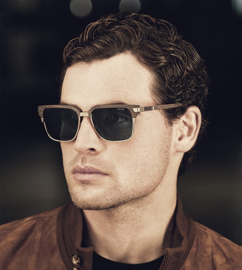 Mann mit kurz gelocktem Haar trägt eine leicht eckige Sonnenbrille mit dunklen Gläsern und braunem Oberrahmen mit bügeln aus Holz und Metall