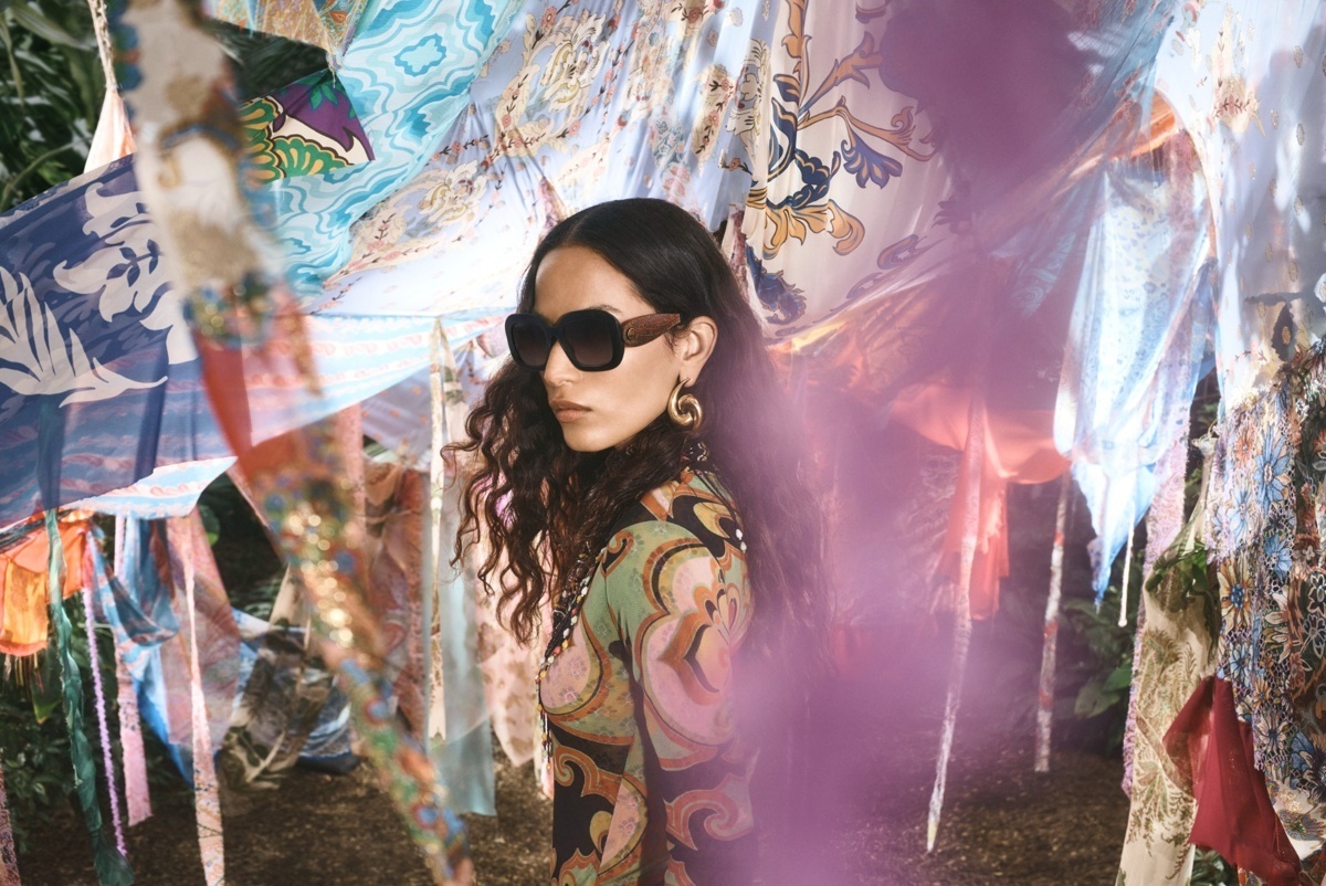 Frau mit Sonnenbrille steht zwischen farbenfrohen Stoffbahnen im Freien