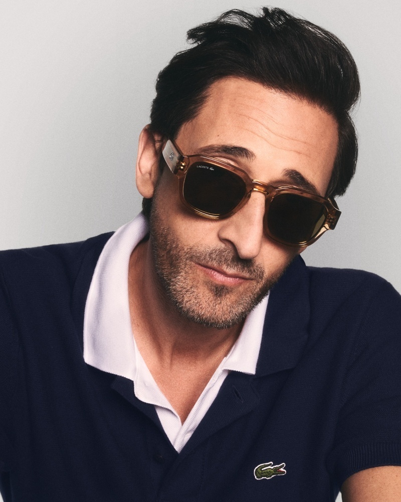 Der Schauspieler Adrien Brody mit Sonnenbrille blickt nach unten und trägt ein dunkelblaues Poloshirt mit weißem Kragen

