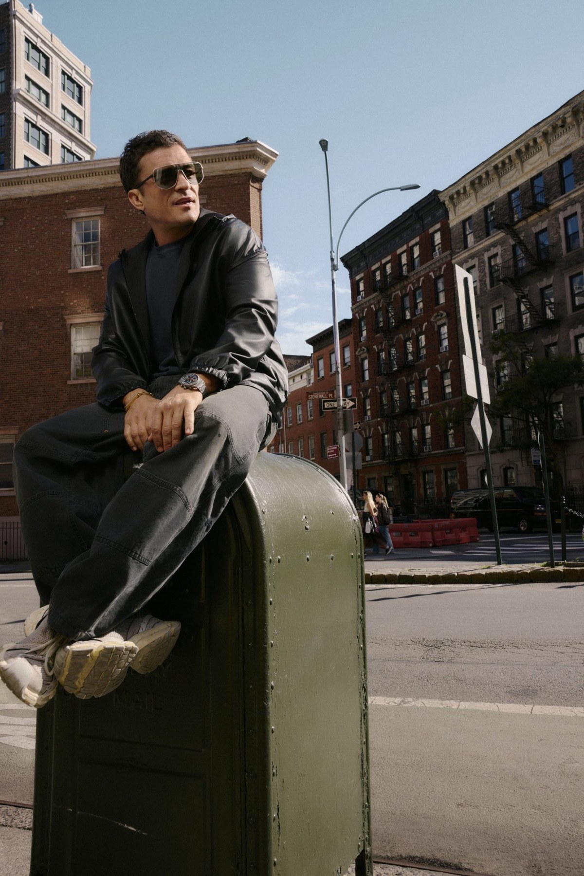 Orlando Bloom sitzt in urbaner Umgebung und trägt eine großflächige Porsche Design Shield-Sonnenbrille aus Titan