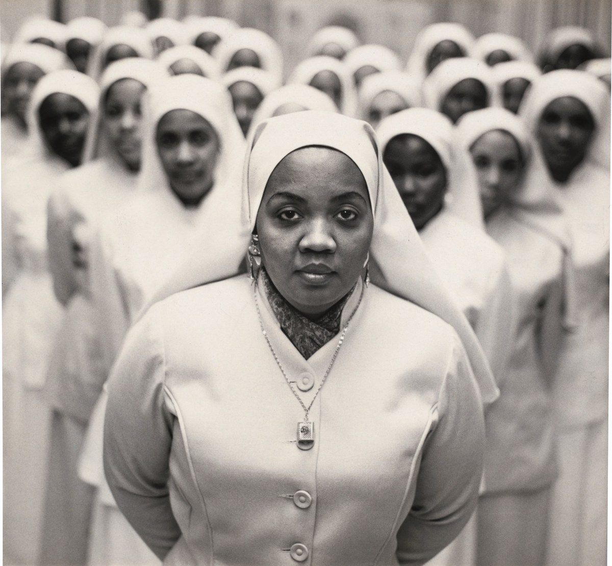 Schwarzweißfotografie einer Gruppe afroamerikanischer Krankenschwestern in weißen Uniformen und Hauben. Die Frau im Vordergrund blickt direkt in die Kamera.