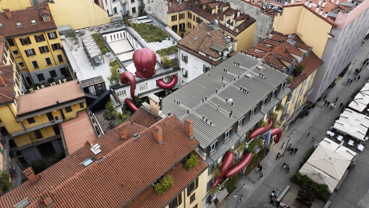 Luftaufnahme eines Mailänder Innenhofs mit rotem, aufblasbarem Oktopus, dessen Tentakel sich über Dach und Fassade eines Gebäudes am 10 Corso Como ziehen.