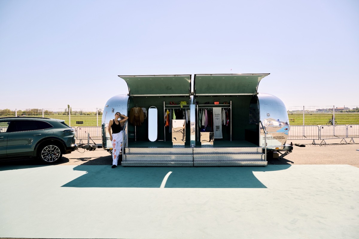 Toni Garrn steht vor einer geöffneten Airstream-Boutique neben einem Porsche Cayenne auf dem Gelände des Berliner Flughafens Tempelhof