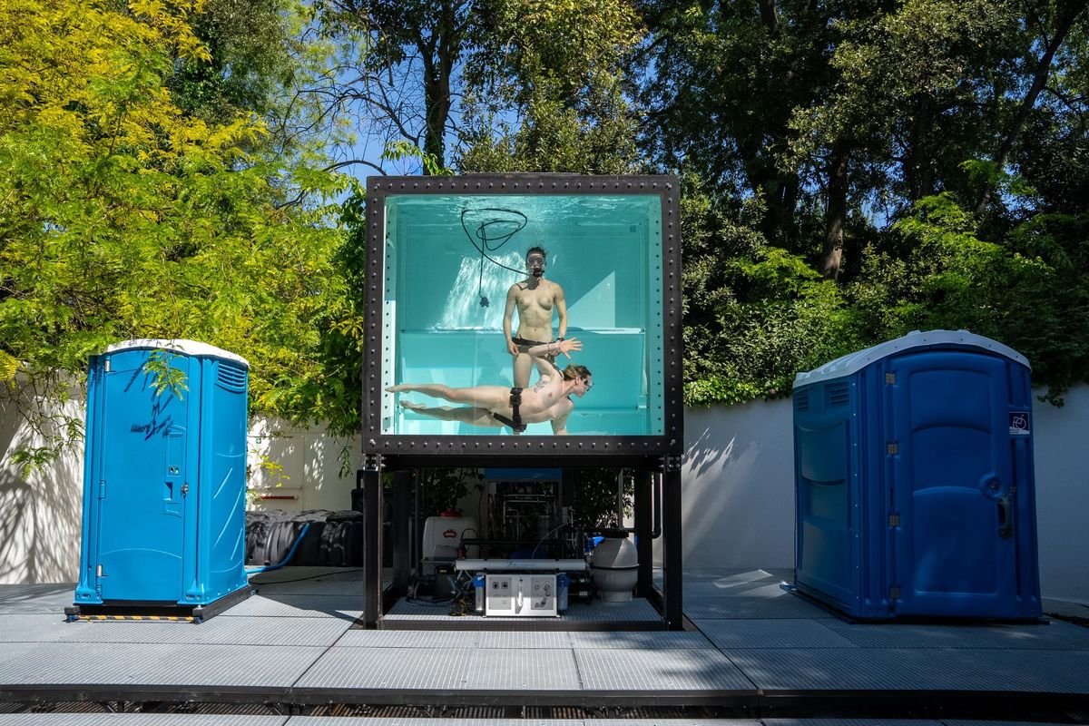 Aquarium mit Performerinnen zwischen zwei mobilen Toiletten im österreichischen Pavillon