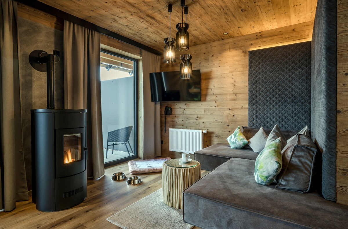 substantial-times-hunderesort-waldeck-02 Wohnbereich eines Chalets im Hunderesort Waldeck mit Kaminofen, Holzinterieur und Hundenäpfen. Das hundefreundliche Hotel im Bayerischen Wald bietet spezielle Unterkünfte für Urlaub mit Hund