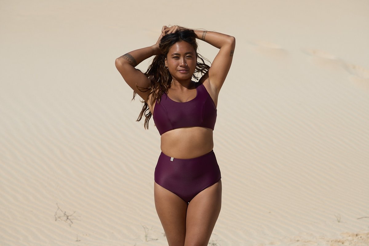 Frau trägt bordeauxfarbenes Bikini-Top und passende High-Waist-Bikinihose von Inaska in einer Dünenlandschaft