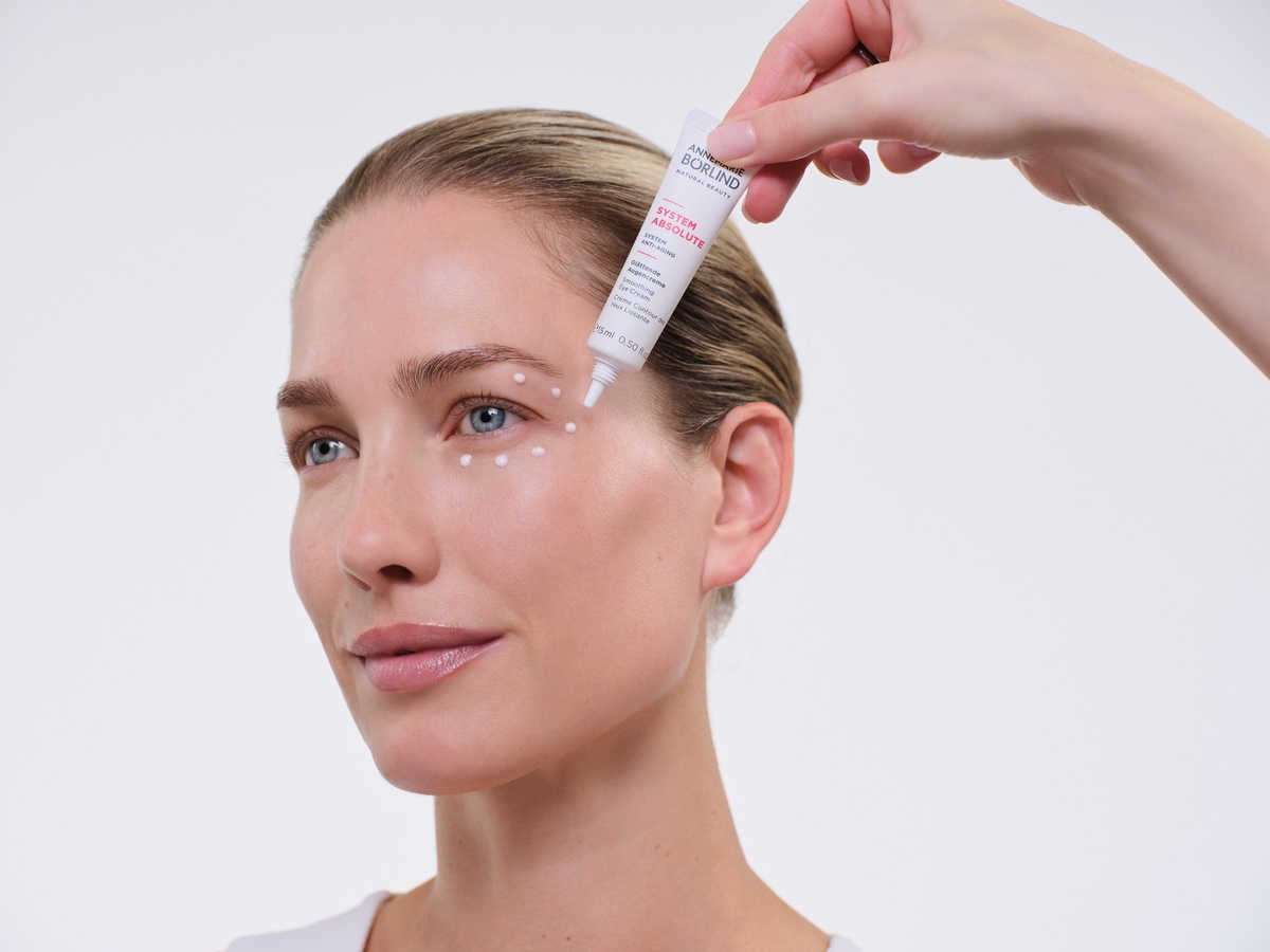 Einem Model wird die „System Absolute Augencreme“ von Annemarie Börlind mit einer Applikatortube um das Auge aufgetragen.