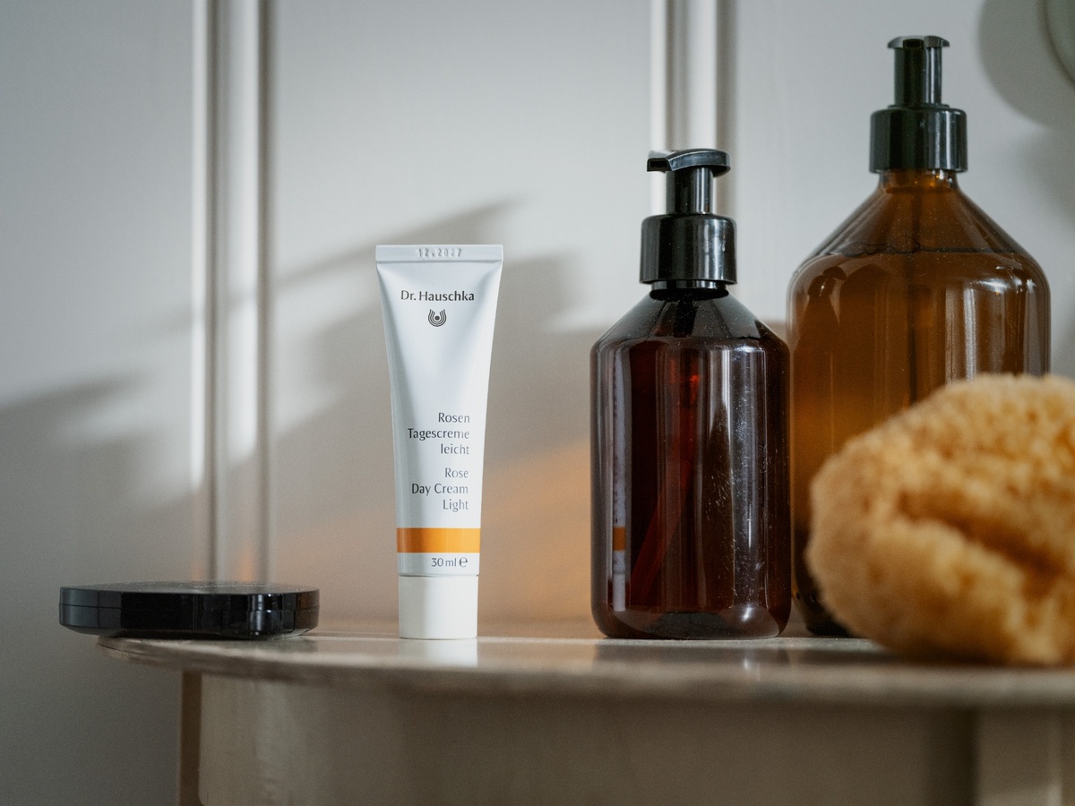Tube Dr.-Hauschka-Rosenpflege in einem Badezimmerregal mit Pumpflaschen und Naturschwamm