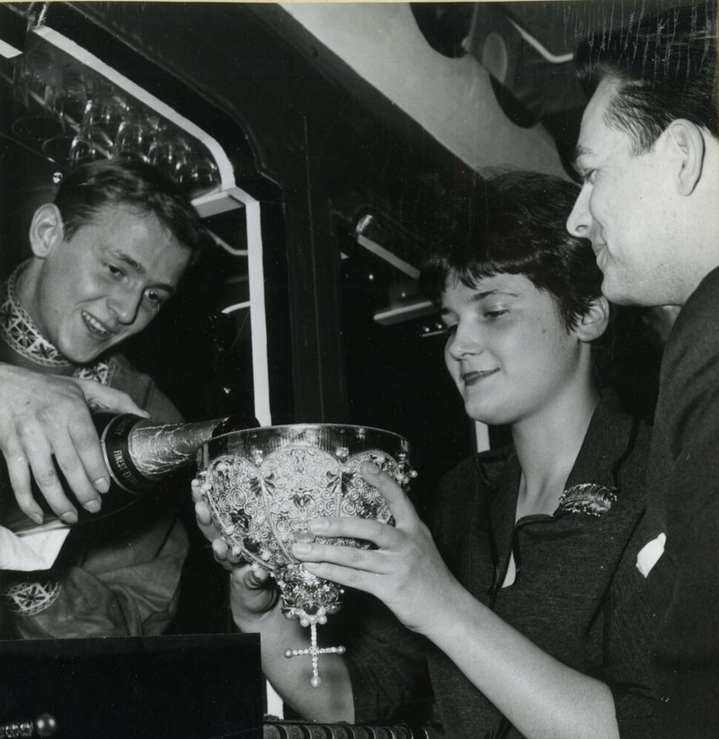 substantial-times-1961-zarenkrone-von-rene-kern-fur-gastronom-helmut-mattner Eine Frau hält die reich verzierte Zarenkrone von René Kern, während ein Mann Champagner hineingießt