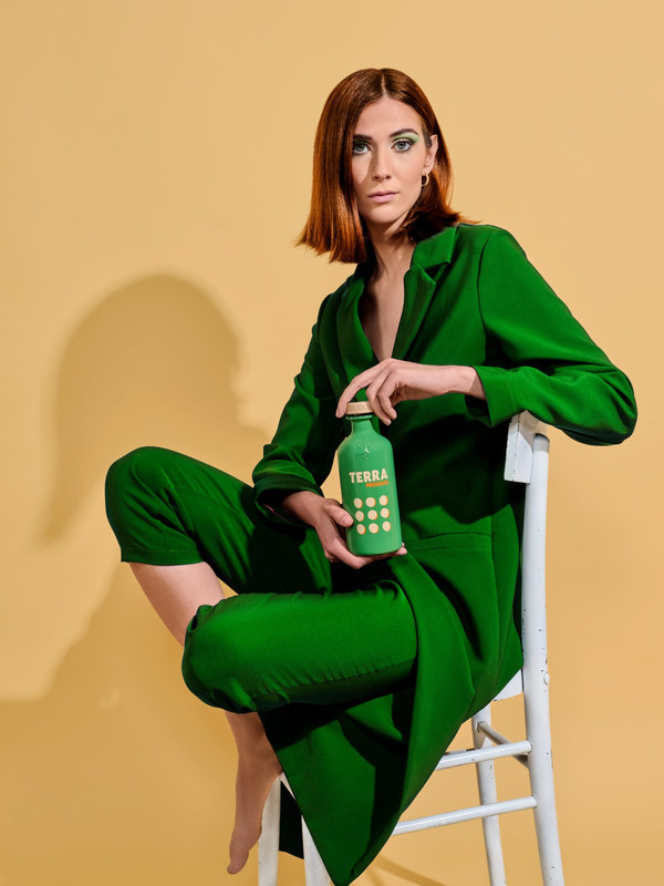 Eine Frau im grünen Hosenanzug hält die grüne Tales-Flasche Terra Pregiata